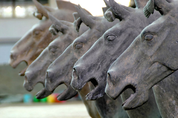 A close-up of bronze horse statues, part of the Terracotta Army. The sculptures feature detailed craftsmanship, open mouths, and expressive eyes.