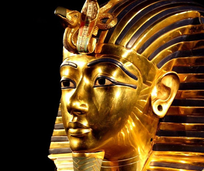 A close-up of King Tutankhamun's golden mask, highlighting its intricate craftsmanship, blue inlays, and the cobra and vulture symbols, representing divine protection and royal authority.
