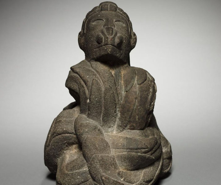 A stone sculpture depicts a bound figure with a solemn expression, intricate carvings, and a restrained posture.