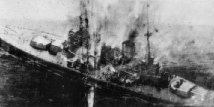 A warship is engulfed in smoke and flames during an attack at sea, likely from aerial or naval bombardment.