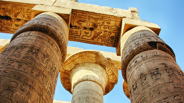Massive ancient Egyptian columns covered in hieroglyphs rise against a clear blue sky.