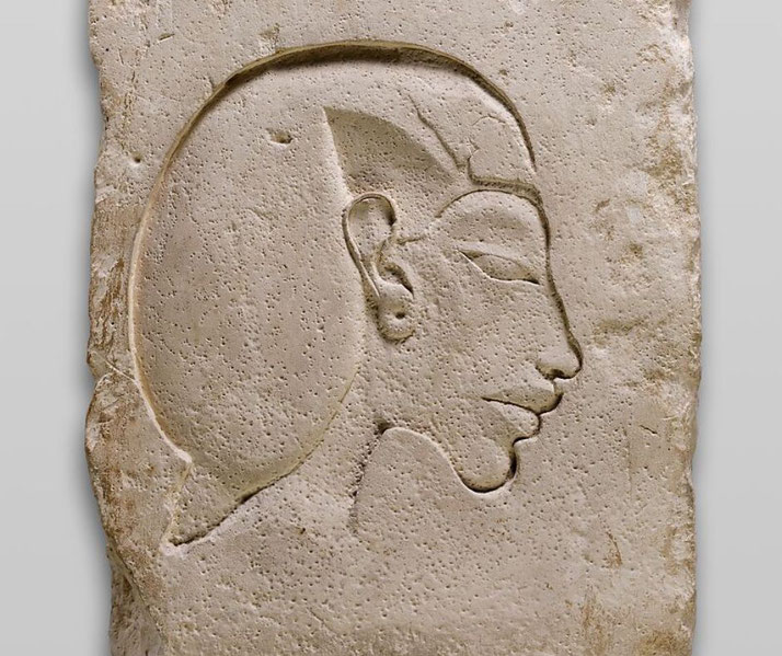 A limestone relief of Pharaoh Akhenaten. The carving features his distinct elongated face, prominent lips, and slanted eyes, reflecting the Amarna artistic style of ancient Egypt.