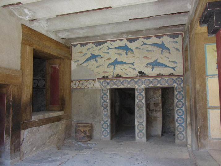 Restored Minoan room with colorful dolphin fresco, decorative columns, and stone flooring inside the Palace of Knossos.