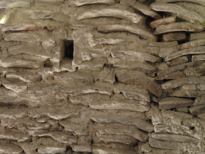 Close-up of an ancient Roman wall with tightly packed curved bricks and a small square opening, showing signs of age and wear.