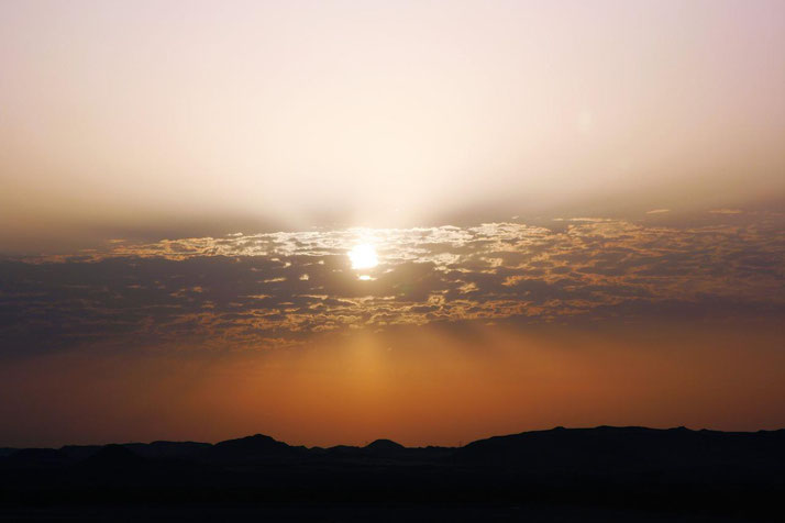 Sunset over a desert landscape with scattered clouds glowing in warm orange and purple hues.