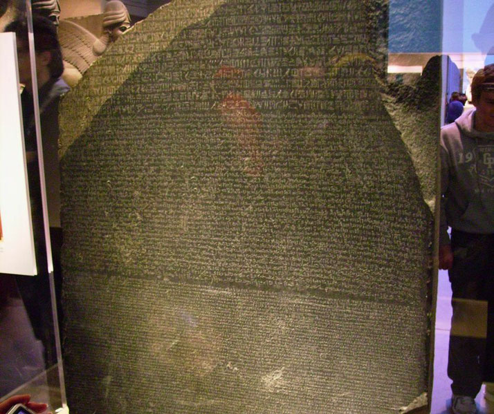 The Rosetta Stone, an ancient slab inscribed with the same text in Egyptian hieroglyphs, Demotic script, and Greek. It was key to deciphering hieroglyphs and is displayed in a museum.