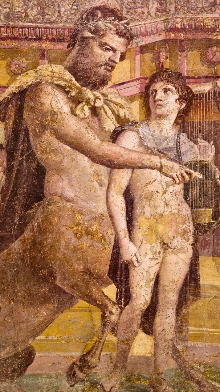 Ancient fresco of a centaur instructing a young man holding a lyre, set against an ornate architectural background, symbolizing mythological mentorship.