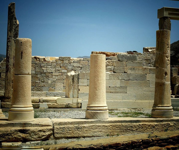 Ancient Greek ruins with partially standing columns and weathered stone walls under a clear blue sky.
