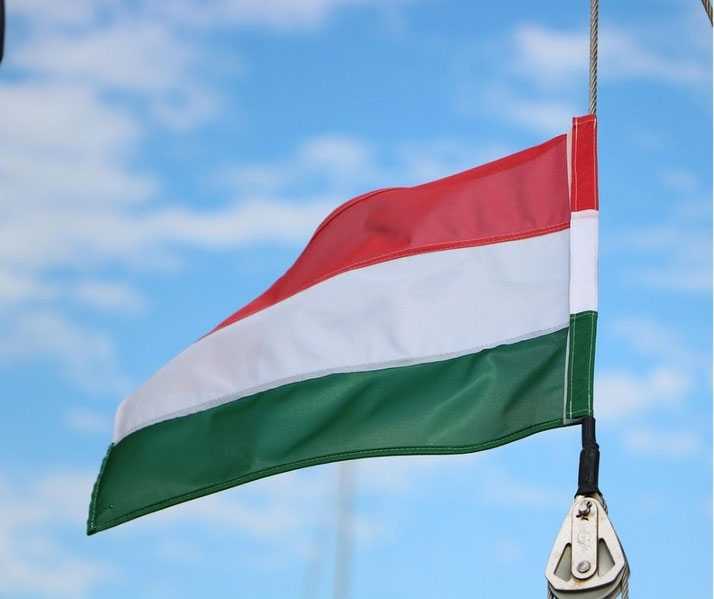 Hungarian national flag waving in the wind against a blue sky with scattered clouds, red white and green stripes visible on a rope mounted pole.