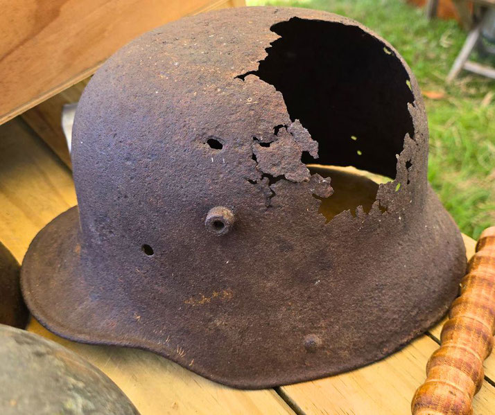 A heavily rusted World War I helmet with a large, jagged hole and several smaller punctures rests on a wooden surface.