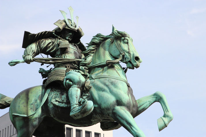 A bronze equestrian statue of a samurai warrior in full armor, wielding a bow. The dynamic pose and intricate details capture the power and tradition of Japan’s feudal era.