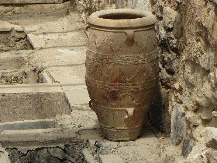 Large ancient clay storage jar with decorative patterns, placed among stone ruins in an archaeological site.