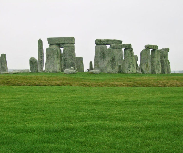 Massive standing stones of Stonehenge rise from a grassy plain under an overcast sky.