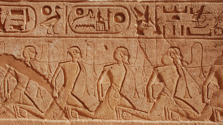 Ancient Egyptian wall carving showing kneeling captives bound with ropes, accompanied by hieroglyphic inscriptions.