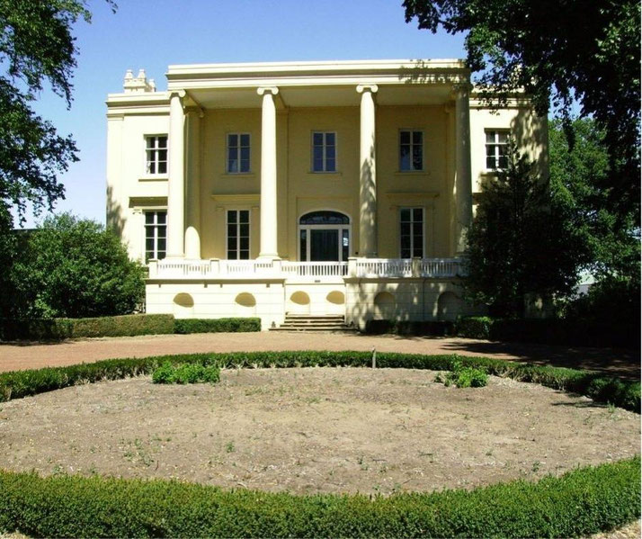 A painted white mansion on dried land surrounded by trees.