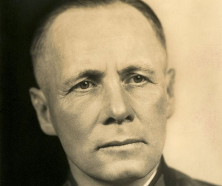 Sepia-toned close-up portrait of a middle-aged man with a serious expression, dressed in a military-style uniform.