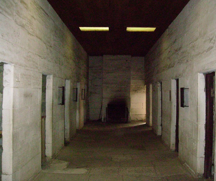 A dimly lit stone corridor with small doorways on either side leads to a darkened area.