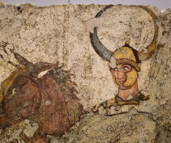 Ancient fresco fragment showing a warrior with a horned helmet and intense gaze, possibly part of a battle or mythological scene.