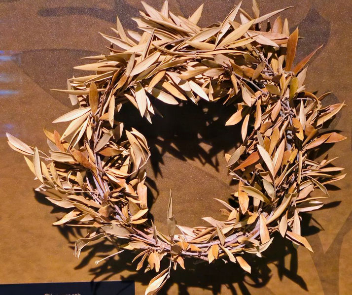 An ancient olive wreath, traditionally awarded to victors in the Olympic Games. The dried leaves and branches highlight its historical significance as a symbol of honor and achievement.