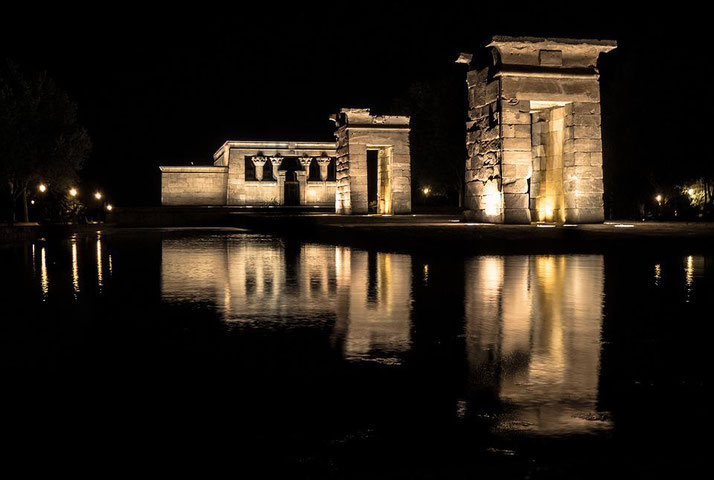 Ancient stone temple illuminated at night with reflections shimmering on a still water surface.