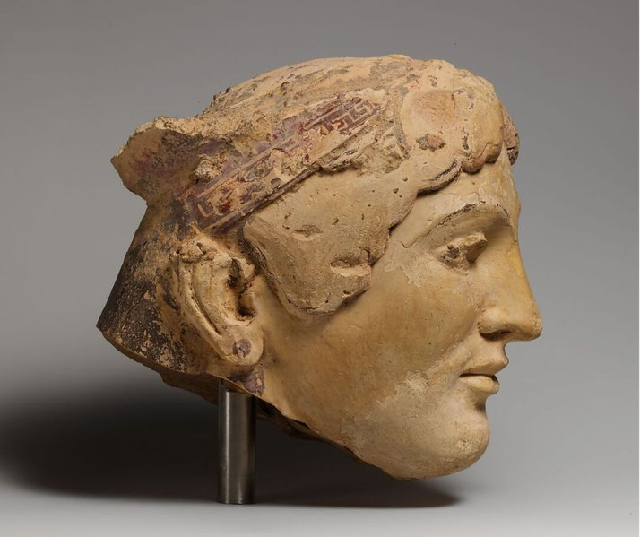 Terracotta sculpture of a large Greek female head with archaic features, likely once part of a sphinx figure used architecturally.