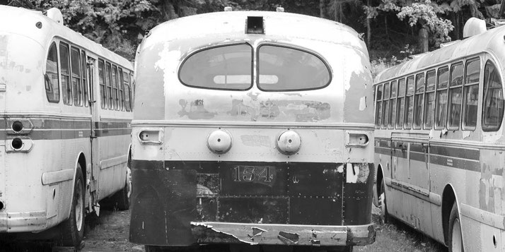 A black-and-white photo of old, worn-out buses parked closely together, showing peeling paint and rust.