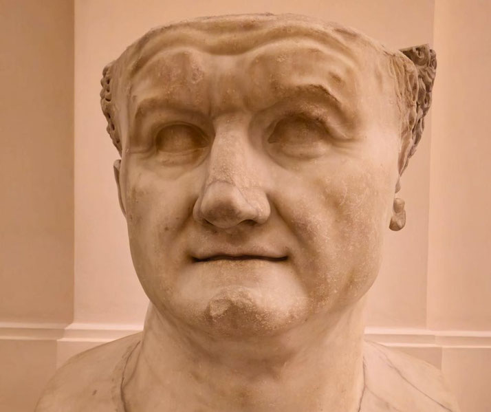 Marble bust of a man with deep-set eyes, prominent brow, and a slight smile, wearing a laurel wreath around his short-cropped hair.
