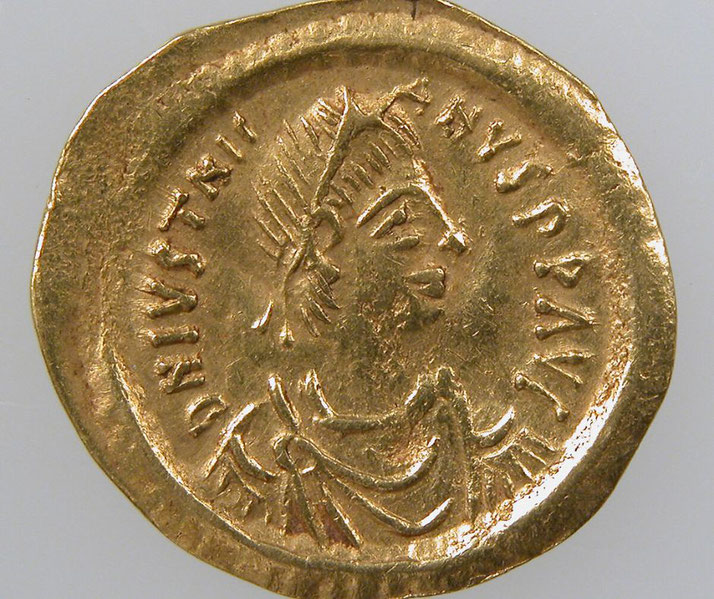 A gold tremissis coin featuring the portrait of Emperor Justinian I, with inscriptions around the edge identifying the emperor and his reign during the Byzantine Empire.