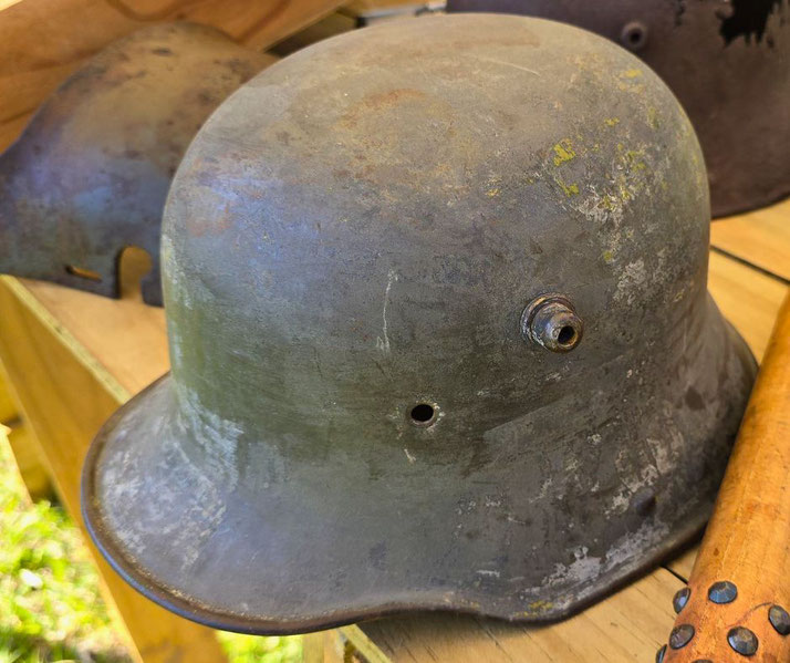 A worn World War I German helmet with a vent and small hole sits on a wooden surface, showing signs of age and use.