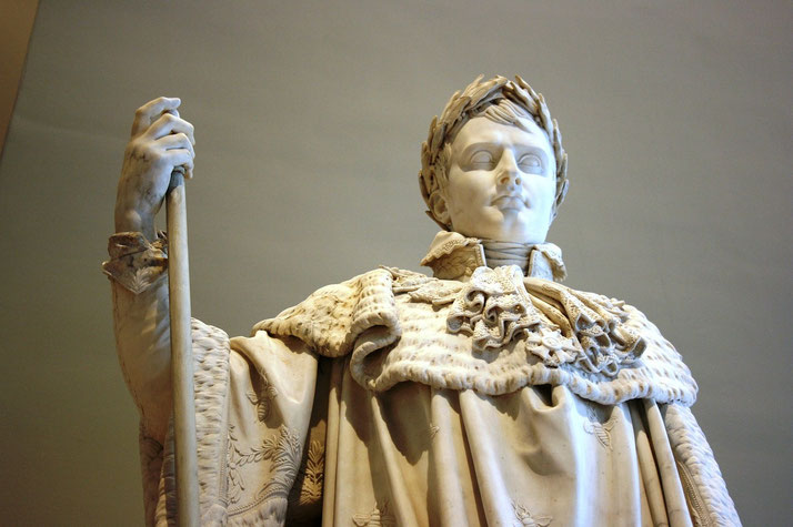 A marble statue of a regal figure in a robe and laurel crown holds a staff, symbolizing authority and leadership.