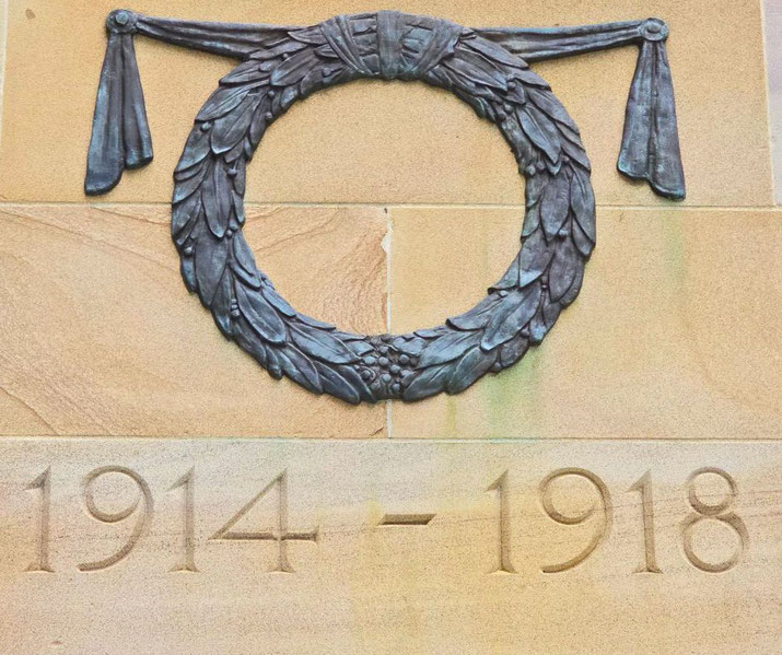 A bronze laurel wreath and dates 1914–1918 are carved into a sandstone wall, marking World War I remembrance.