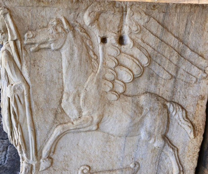 Ancient stone relief depicting Pegasus, the winged horse, with a partially visible robed figure beside it.