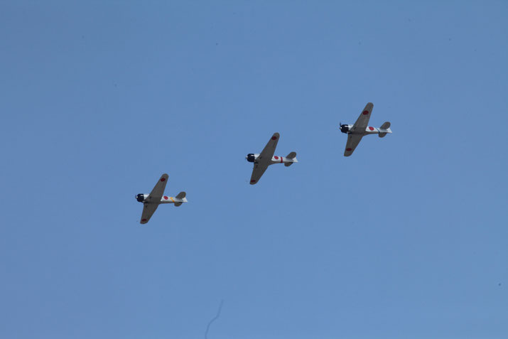 Three vintage Japanese WWII aircraft fly in formation against a clear blue sky, displaying red circle insignias.