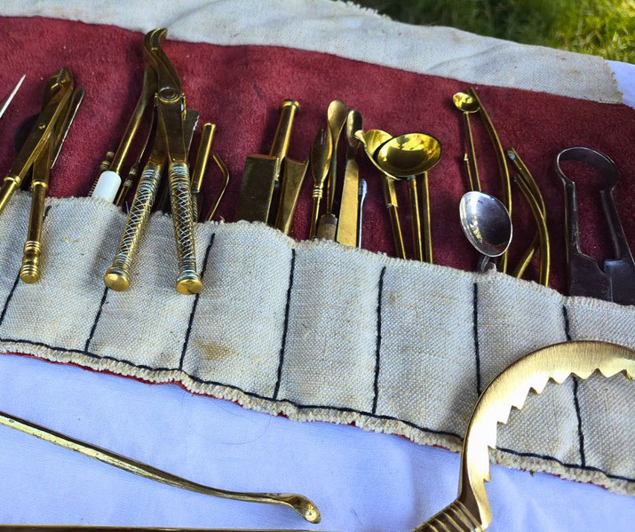 Collection of antique brass and metal medical tools arranged in a fabric roll on a table, possibly for historical reenactment.