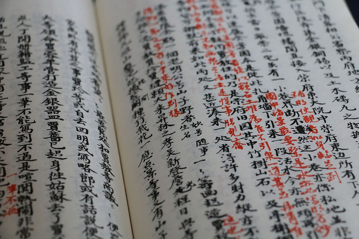 An open book with traditional Chinese calligraphy, written in black ink with red annotations.