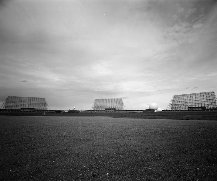 Wide-angle black and white photo of a radar installation with three large grid antennas and a spherical dome structure on a flat, open landscape.