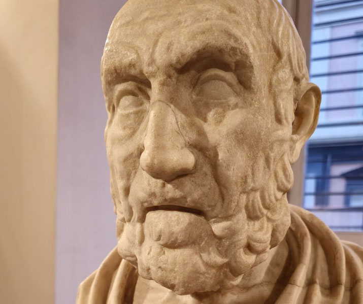 Weathered marble bust of an elderly man with deep wrinkles, a furrowed brow, and a solemn expression, draped in a toga.