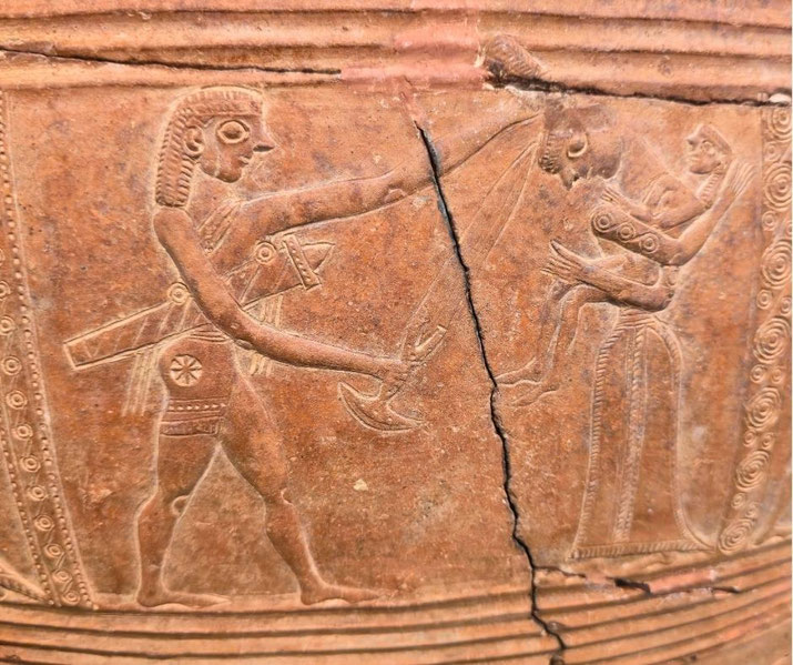 Ancient terracotta relief on the Mykonos Vase depicting a warrior confronting a woman holding a child, with fine carved details and visible restoration cracks.