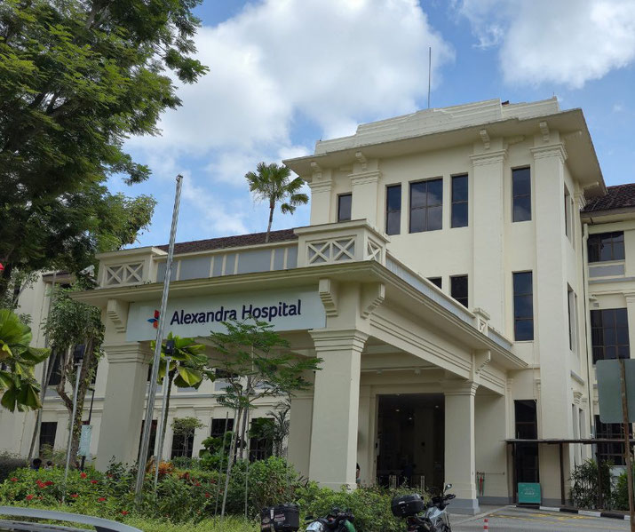 Alexandra Hospital’s cream-colored building with tall windows stands under a blue sky with scattered clouds.