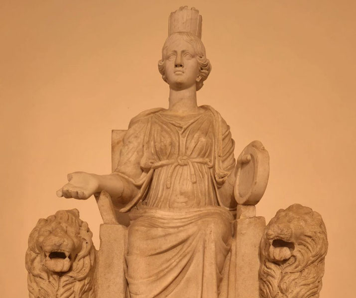 Seated female statue wearing a crown, holding a drum, flanked by two roaring lions, symbolizing power and divinity.