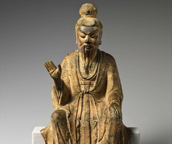 An ancient statue of a Daoist Immortal, likely Laozi, seated with a serene expression, long beard, and flowing robes, symbolizing wisdom and spiritual authority.