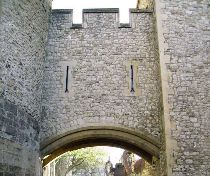 Stone castle wall with a central arched passageway and two narrow vertical arrow slits above.