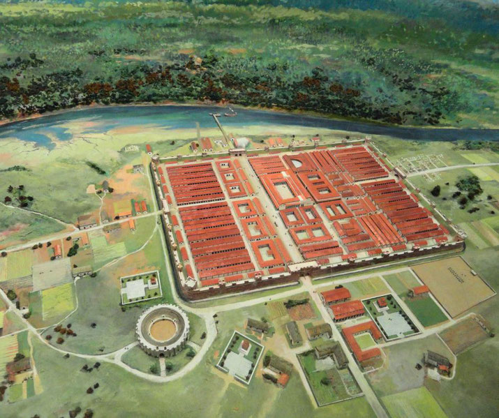 A detailed model shows a Roman military fort with red-roofed buildings, a surrounding wall, nearby amphitheater, and adjacent river and countryside.