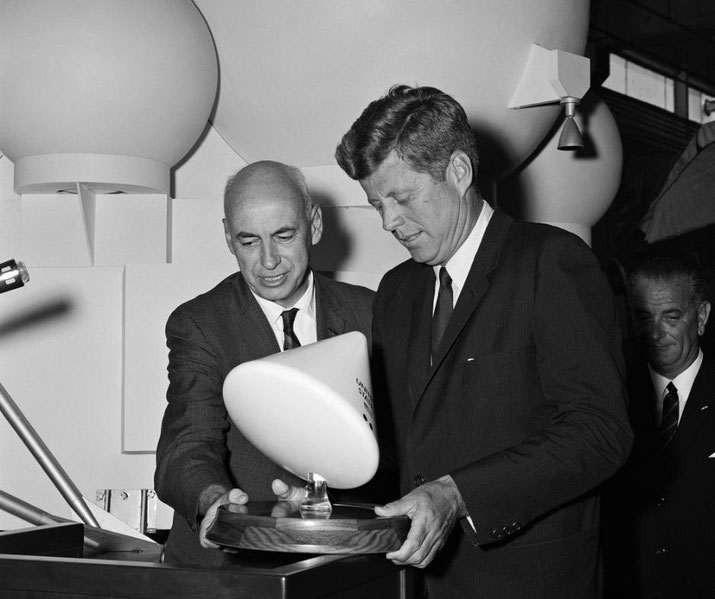 President John F. Kennedy look at a small model of the Apollo Command Module