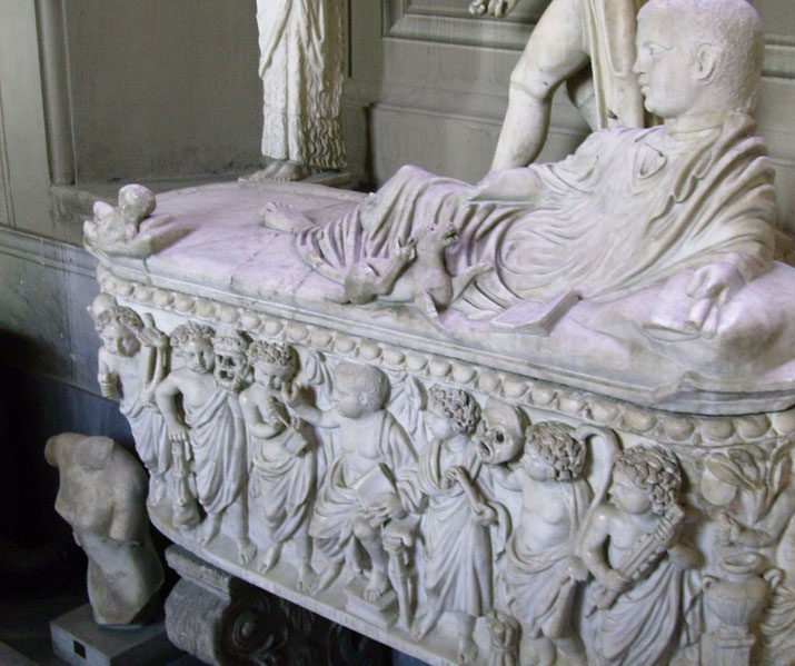 Marble sarcophagus with a reclining figure on the lid and a frieze of children and mythological figures carved around the base.