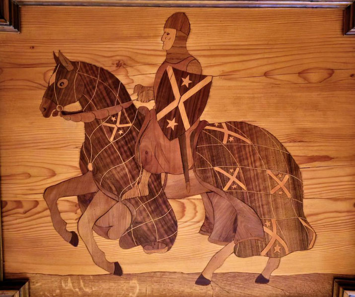 An intricate wooden inlay artwork showing a medieval knight on horseback, adorned with a shield and patterned barding, framed in a polished wooden setting.
