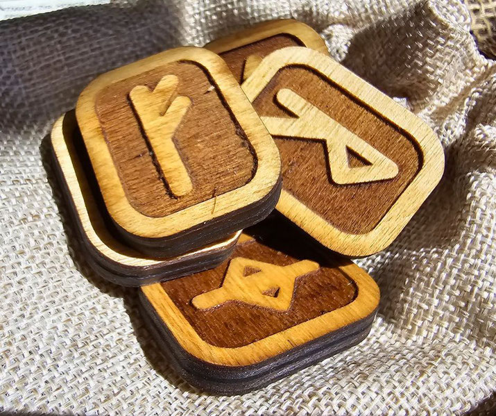 Wooden tiles with carved rune symbols, placed on a textured burlap cloth. The runes appear to have a Viking or Nordic design, combining a rustic aesthetic with detailed craftsmanship.