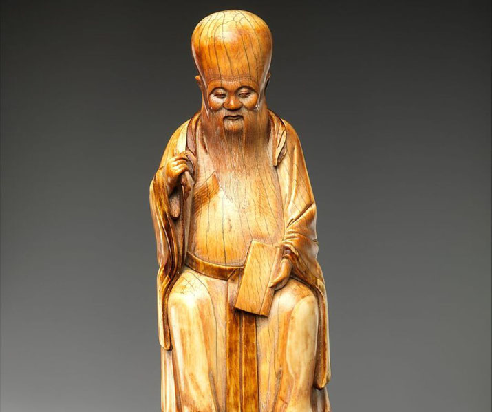 A carved statue of Shouxing, the Chinese Stellar God of Immortality, depicted with an elongated forehead, long beard, and a scroll.