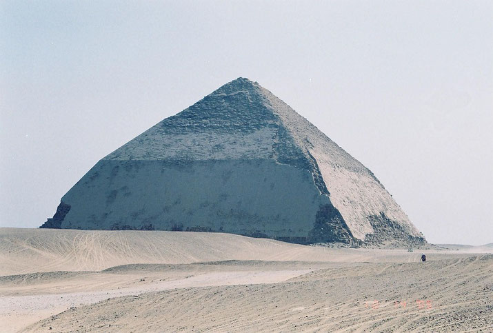 The Bent Pyramid stands alone in the desert, its distinct change in angle visible halfway up the structure under a hazy sky.