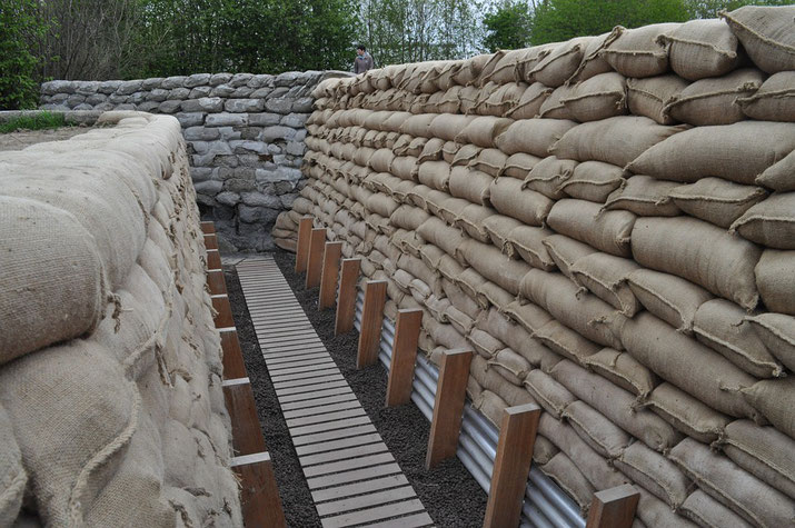 A restored trench lined with stacked sandbags and a wooden walkway, showing clean and well-maintained construction in a historical site.